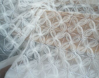 May include: White sheer fabric with a delicate floral pattern. The fabric is embellished with small white beads, creating a subtle shimmer.