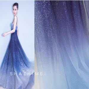 Könnte beinhalten: Eine Frau in einem bodenlangen Kleid mit einem Farbverlauf von Blau, von tiefem Marineblau bis zu einem weichen, hellen Blau. Das Kleid hat einen funkelnden, glitzernden Effekt. Der Markenname "SHAZHIMEI" ist sichtbar.