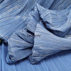 May include: Close-up of light blue pleated fabric with a metallic sheen. The fabric is folded and gathered, creating a textured surface. The text "Lacemily" is visible on the fabric.