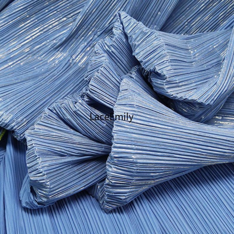 May include: Close-up of light blue pleated fabric with a metallic sheen. The fabric is folded and gathered, creating a textured surface. The text "Lacemily" is visible on the fabric.