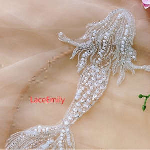 Puede incluir: Una aplicación de sirena de cuentas blancas con un diseño detallado. La aplicación está sobre una tela de tul beige. LaceEmily está escrito en rojo en la tela.