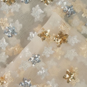 May include: Beige tulle fabric with gold, silver, and white star-shaped sequins.
