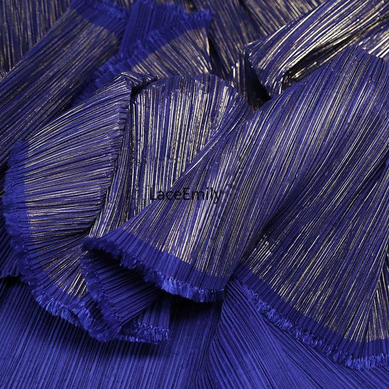 May include: Close-up of a vibrant blue pleated fabric with metallic gold stripes. The fabric is bunched and folded, showcasing its texture and sheen. The edges are frayed, adding a touch of detail.