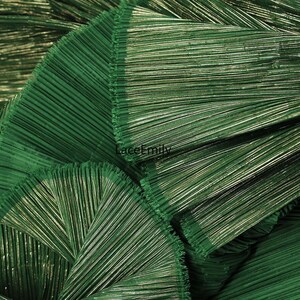 May include: Close-up of a folded, textured fabric in a deep green hue. The fabric has a pleated design with metallic threads woven throughout, creating a shimmering effect. The text "LaceEmily" is visible in the image.