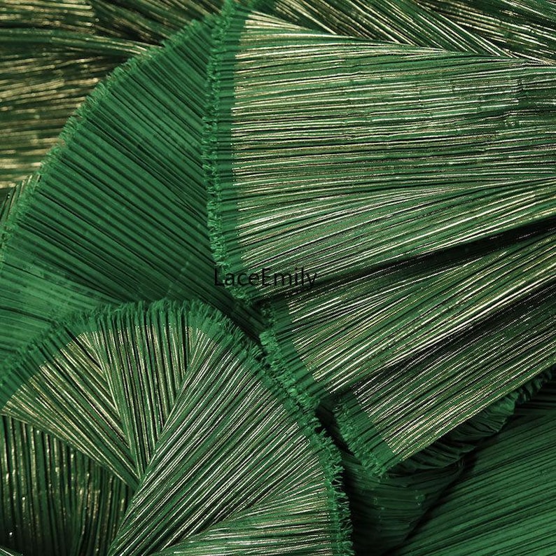 May include: Close-up of a folded, textured fabric in a deep green hue. The fabric has a pleated design with metallic threads woven throughout, creating a shimmering effect. The text "LaceEmily" is visible in the image.