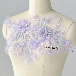 May include: A delicate lavender floral applique with pearl accents on a sheer tulle fabric. The applique features a cluster of flowers and leaves, with a subtle pink undertone. The text "LaceEmily" is visible in the bottom right corner.