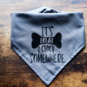 Puede incluir: Bandana gris para perro con texto negro que dice "It's Treat O'Clock Somewhere" con un gráfico de hueso negro.