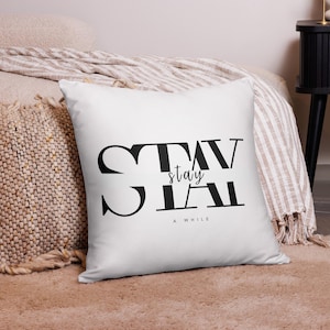 May include: White throw pillow with black text that reads "STAY A WHILE" with the word "stay" in a smaller font and inside the word "STAY".