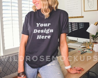 May include: A woman wearing a charcoal gray t-shirt with the text "Your Design Here" printed on the front. She is sitting at a table with a computer and other office supplies.