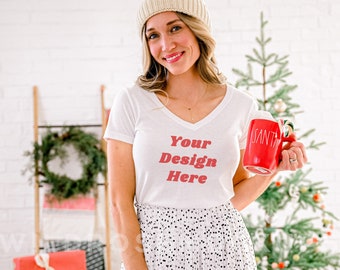 Puede incluir: Una camiseta blanca de cuello en V con el texto "Your Design Here" en letras rojas. La camiseta la lleva puesta una persona que sostiene una taza roja con la palabra "Santa" en ella.