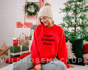 May include: A red sweatshirt with the text "Your Design Here" in black. The sweatshirt is being worn by a person with a white knit beanie and sitting on a white fluffy rug in front of a Christmas tree.