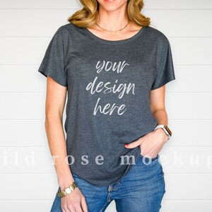 May include: A dark charcoal grey short-sleeved t-shirt with a scoop neckline. The front of the shirt features the white text "your design here" in a cursive script font. The shirt is paired with blue denim jeans and a white smartwatch on the wrist.