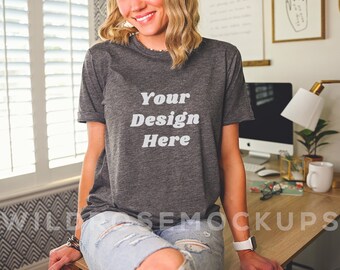 May include: A woman wearing a gray t-shirt with the text "Your Design Here" printed on the front. She is sitting at a table with a computer and other items.