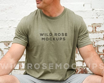 May include: A man wearing a green t-shirt with the text "WILD ROSE MOCKUPS" printed on the front. The shirt is a relaxed fit and has a crew neck.