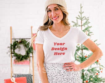 Puede incluir: Una camiseta blanca de cuello en V con el texto "Your Design Here" en letras rojas. La camiseta la lleva puesta una persona con un gorro de punto blanco y una falda de lunares blancos y negros.