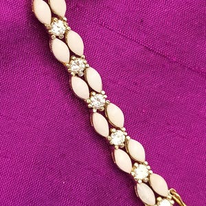 Könnte beinhalten: Goldfarbenes Armband mit abwechselnd ovalen, hellrosa Steinen und klaren, runden Kristallen. Der Hintergrund ist ein leuchtend violetter Stoff. Der Verschluss ist ebenfalls goldfarben. Ca. 18 cm lang.