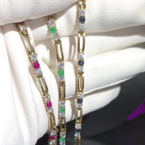 May include: Three gold bracelets with alternating gemstones. One bracelet features rubies and diamonds, another emeralds and diamonds, and the third sapphires and diamonds. The bracelets are displayed against a white background.