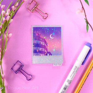 May include: A holographic sticker featuring a cityscape at night with a crescent moon and stars. The sticker has a white border and the words "Peel Tab" are printed on the bottom right corner.