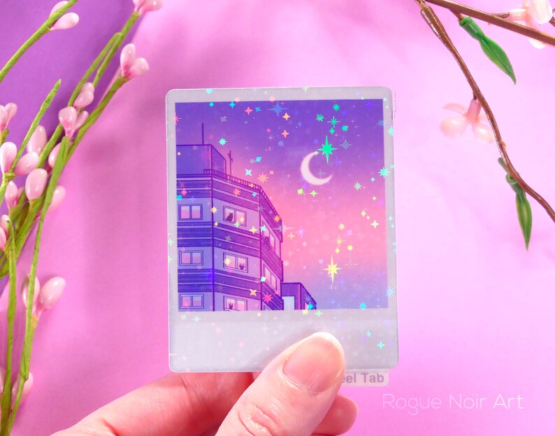 May include: A holographic sticker featuring a cityscape with a crescent moon and stars in the sky. The sticker is in a Polaroid frame with a white border and a glittery texture.