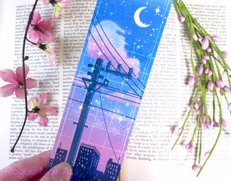 May include: A holographic bookmark featuring a cityscape at night with a crescent moon and stars in the sky. The cityscape is outlined in pink and blue, with a power line running through the center of the image.