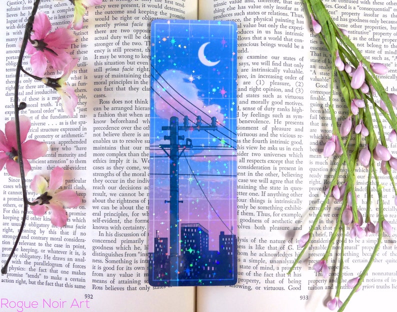 May include: A holographic bookmark with a cityscape silhouette, a crescent moon, and stars against a blue and pink sky. The bookmark has a glittery, iridescent finish.