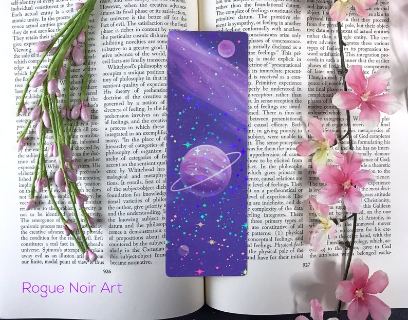 May include: A purple and blue bookmark with a galaxy design. The bookmark features a large planet with a ring, a smaller planet, and a scattering of stars. The bookmark is perfect for adding a touch of whimsy to any book.