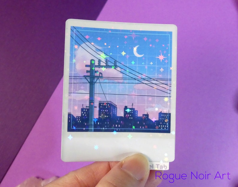Puede incluir: Una pegatina hologr&aacute;fica que representa una ciudad nocturna con una luna creciente y estrellas. La pegatina tiene un acabado brillante e iridiscente.