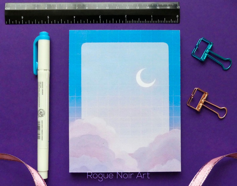 May include: A blue and white sticker with a crescent moon and clouds. The sticker has a grid pattern and the text "Rogue Noir Art" at the bottom.