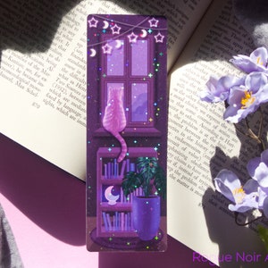 May include: A purple and pink holographic bookmark featuring a cat sitting on a bookshelf with a potted plant and a crescent moon. The bookmark has a glittery finish and stars hanging from the top.