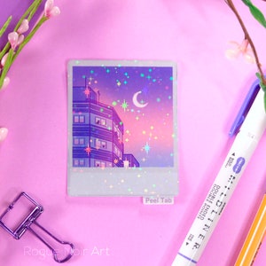 May include: A holographic sticker featuring a cityscape at night with a crescent moon and stars. The sticker has a peel tab and says "Peel Tab" at the bottom.