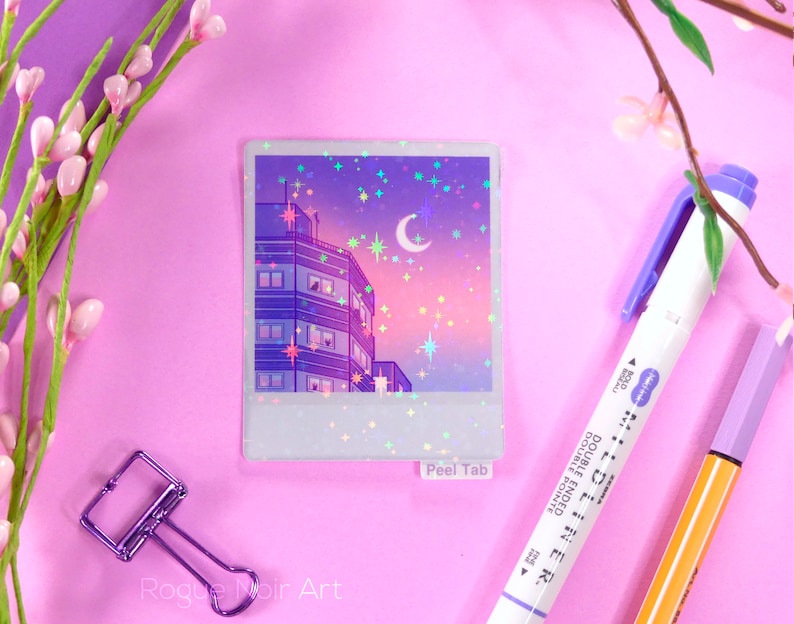 May include: A holographic sticker featuring a cityscape at night with a crescent moon and stars. The sticker has a peel tab and says "Peel Tab" at the bottom.