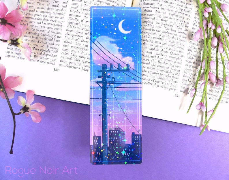 May include: A holographic bookmark with a cityscape silhouette, a crescent moon, and stars against a blue and purple gradient sky. The bookmark has a grid pattern and a holographic finish.