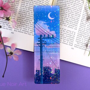 May include: A blue and pink city skyline with a crescent moon and stars. The image is a holographic bookmark with a grid pattern and glitter accents.