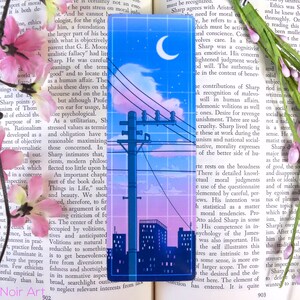 May include: A blue and pink aesthetic bookmark with a cityscape silhouette, a crescent moon, and a power line with birds. The bookmark has a grid pattern overlay.