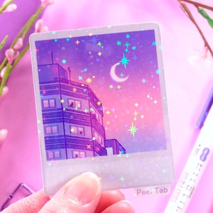 May include: A holographic sticker featuring a purple and pink cityscape with a crescent moon and stars. The sticker has a peel tab that says "Peel Tab".