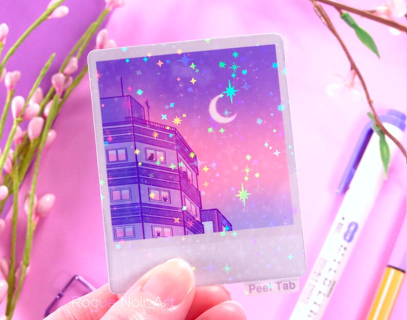 May include: A holographic sticker featuring a purple and pink cityscape with a crescent moon and stars. The sticker has a peel tab that says "Peel Tab".