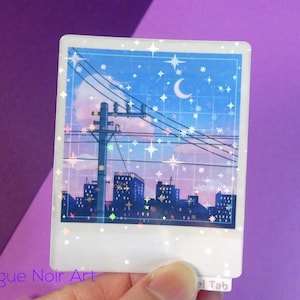 Puede incluir: Una pegatina hologr&aacute;fica que representa una ciudad nocturna con una luna creciente y estrellas en el cielo. La pegatina tiene un borde blanco y un marco de estilo Polaroid.