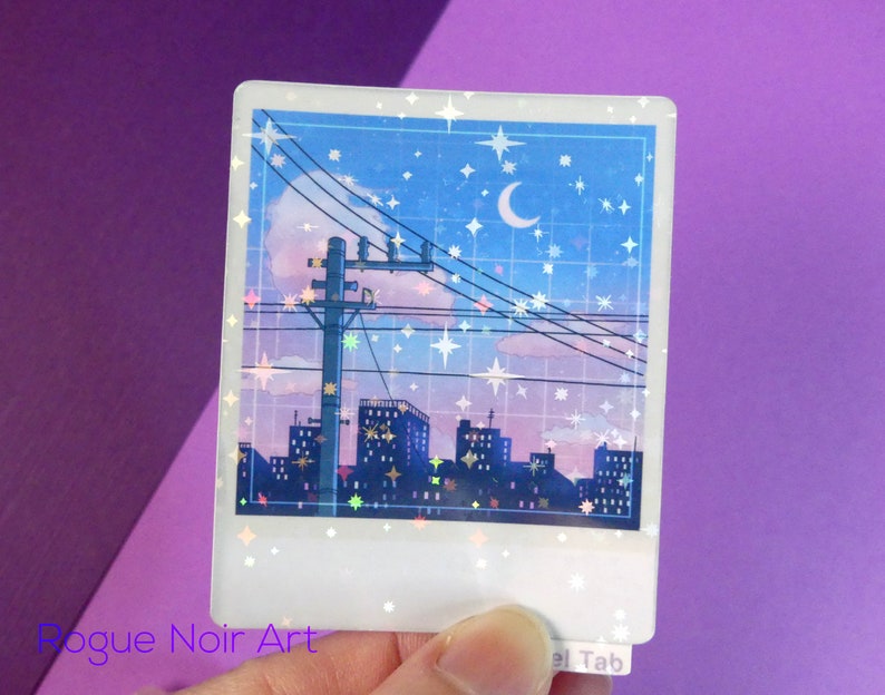 Puede incluir: Una pegatina hologr&aacute;fica que representa una ciudad nocturna con una luna creciente y estrellas en el cielo. La pegatina tiene un borde blanco y un marco de estilo Polaroid.