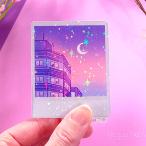 May include: A holographic sticker featuring a purple and pink cityscape with a crescent moon and stars. The sticker is in the shape of a Polaroid photo.