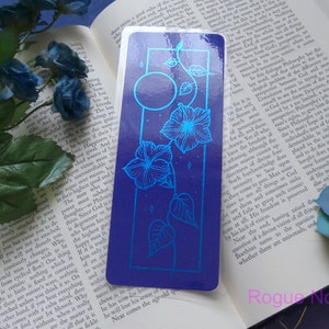 May include: A blue and silver bookmark with a floral design and a moon. The bookmark has a blue background with silver flowers and a moon. The bookmark is a great way to mark your place in a book.