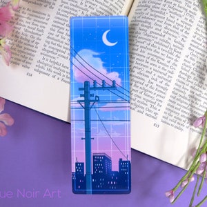 May include: A city skyline at night with a crescent moon in the sky. The sky is a gradient of pink, purple, and blue. There are power lines and a tall pole with a transformer. The city buildings are silhouetted against the sky.