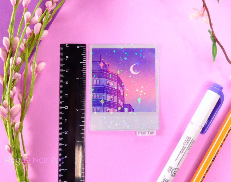 May include: A holographic sticker featuring a cityscape at night with a crescent moon and stars. The sticker has a white border and the words "Peel Tab" at the bottom.