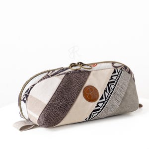 Peut inclure: Une trousse rectangulaire avec un motif patchwork. L'étui présente une variété de tissus aux tons neutres, dont le beige, le marron et le gris, avec une fermeture éclair et un petit patch en cuir. La trousse mesure environ 20 cm de long.