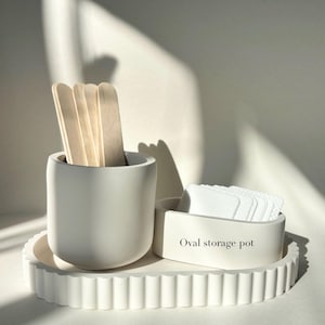 May include: A white storage set with a fluted-edge tray, a cylindrical container holding wooden sticks, and an oval container labelled "Oval storage pot" containing white pads. Ideal for organizing small items.