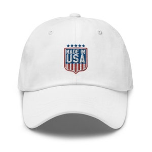 Könnte beinhalten: Weiße Baseballkappe mit einem gestickten Schild, das den Text "MADE IN USA" in blauer und roter Schrift mit fünf Sternen über dem Text zeigt.