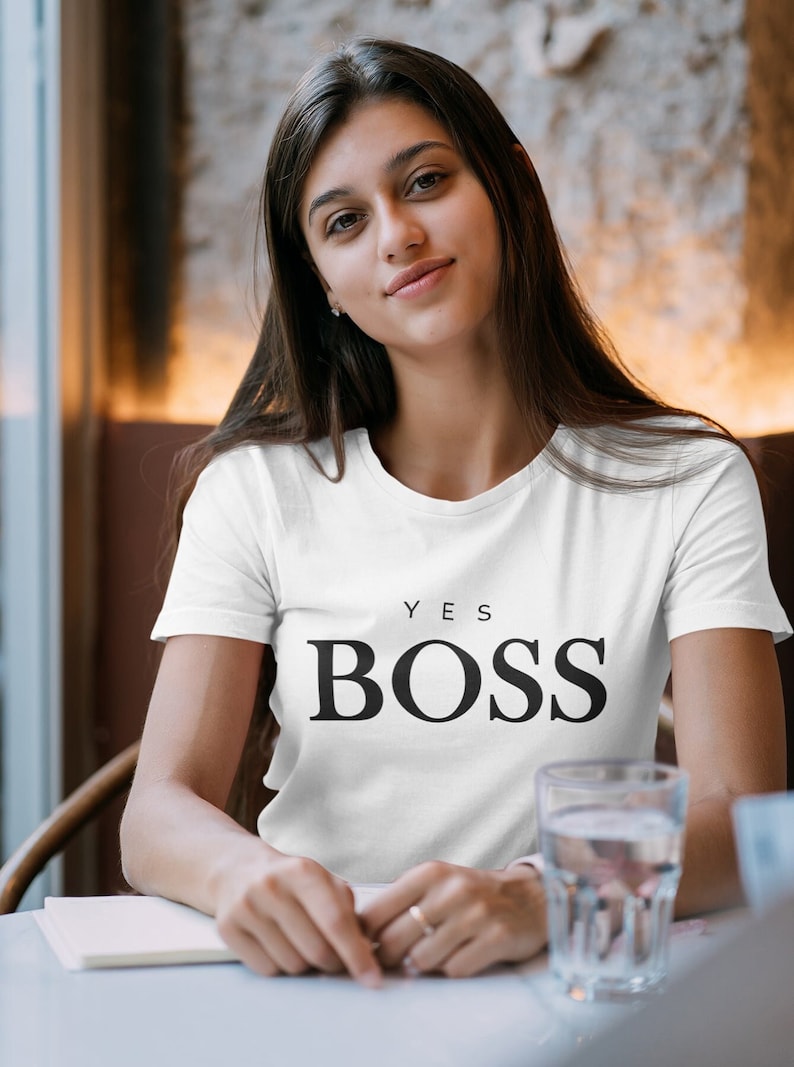 Może przedstawiać: Biała koszulka z nadrukiem "YES BOSS" w kolorze czarnym.