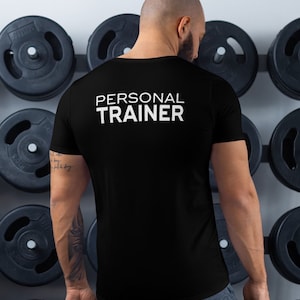 K&ouml;nnte beinhalten: Ein schwarzes T-Shirt mit dem Text "PERSONAL TRAINER" in wei&szlig; auf der R&uuml;ckseite.