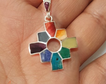 May include: A silver pendant with a colorful, multi-faceted, geometric design. The pendant is shaped like a cross with a circle in the center. The colors of the stones are red, orange, yellow, green, blue, purple, and black.