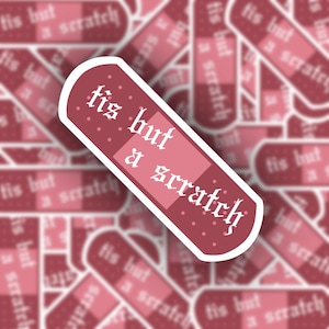May include: A pink and white band-aid sticker with the text "tis but a scratch" in a gothic font.