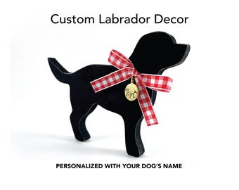 May include: Black Labrador silhouette with a red and white gingham bow and a gold charm. The text "Custom Labrador Decor" and "Personalized with your dog's name" are displayed above and below the dog silhouette.